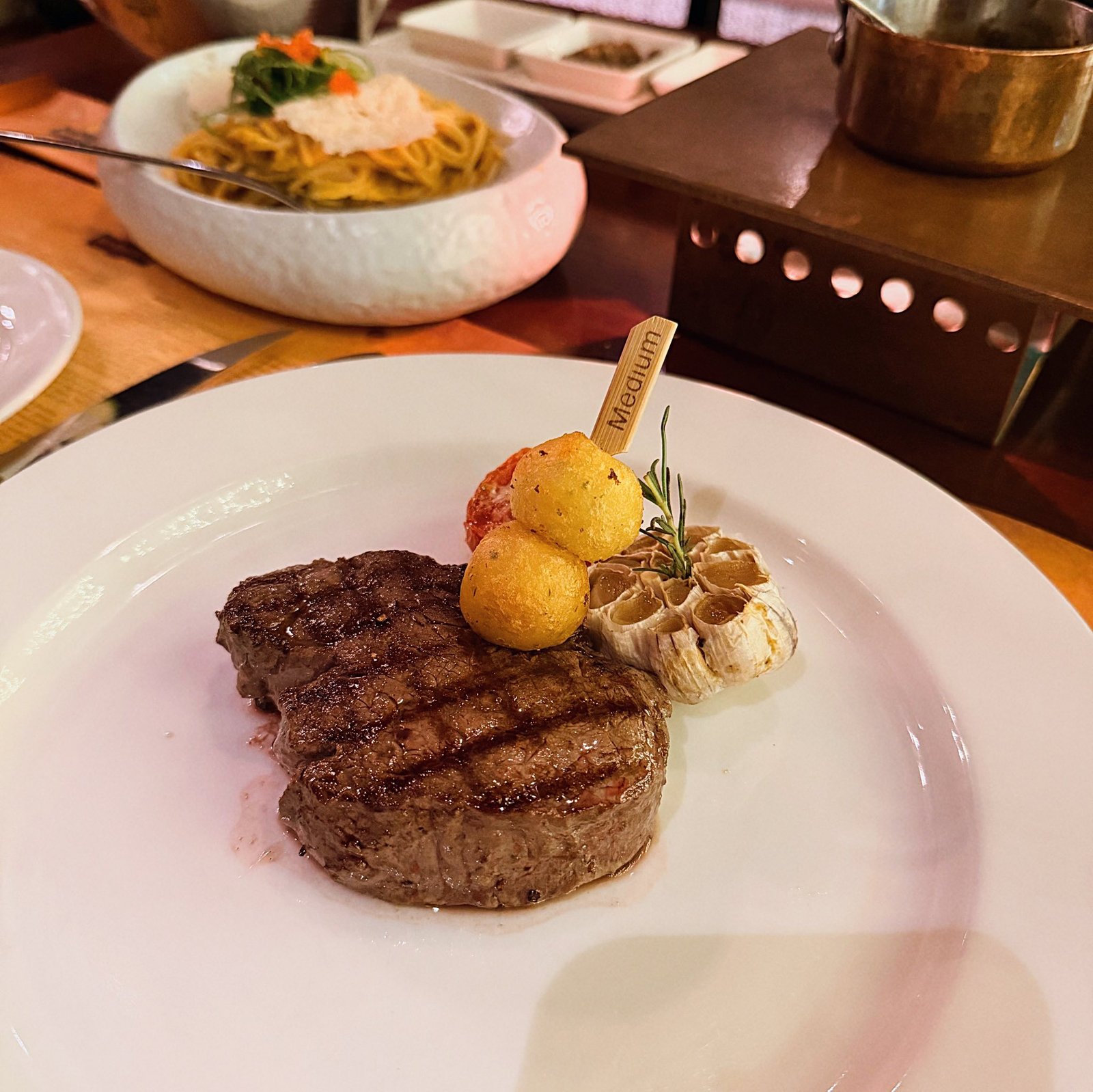 Grilled steak plated with roasted garlic, potato croquettes, and rosemary